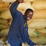 Photo d'un jeune homme d'origine africaine souriant devant des sacs de fèves de cacao. 