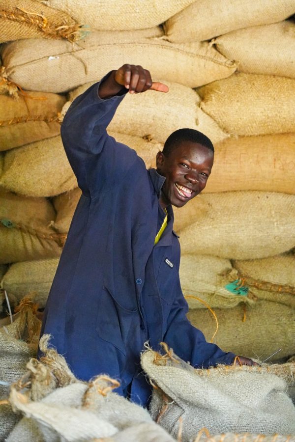 Photo d'un jeune homme d'origine africaine souriant devant des sacs de fèves de cacao.